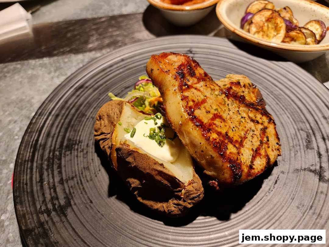 A grilled pork chop served with a baked potato and salad on a black plate.