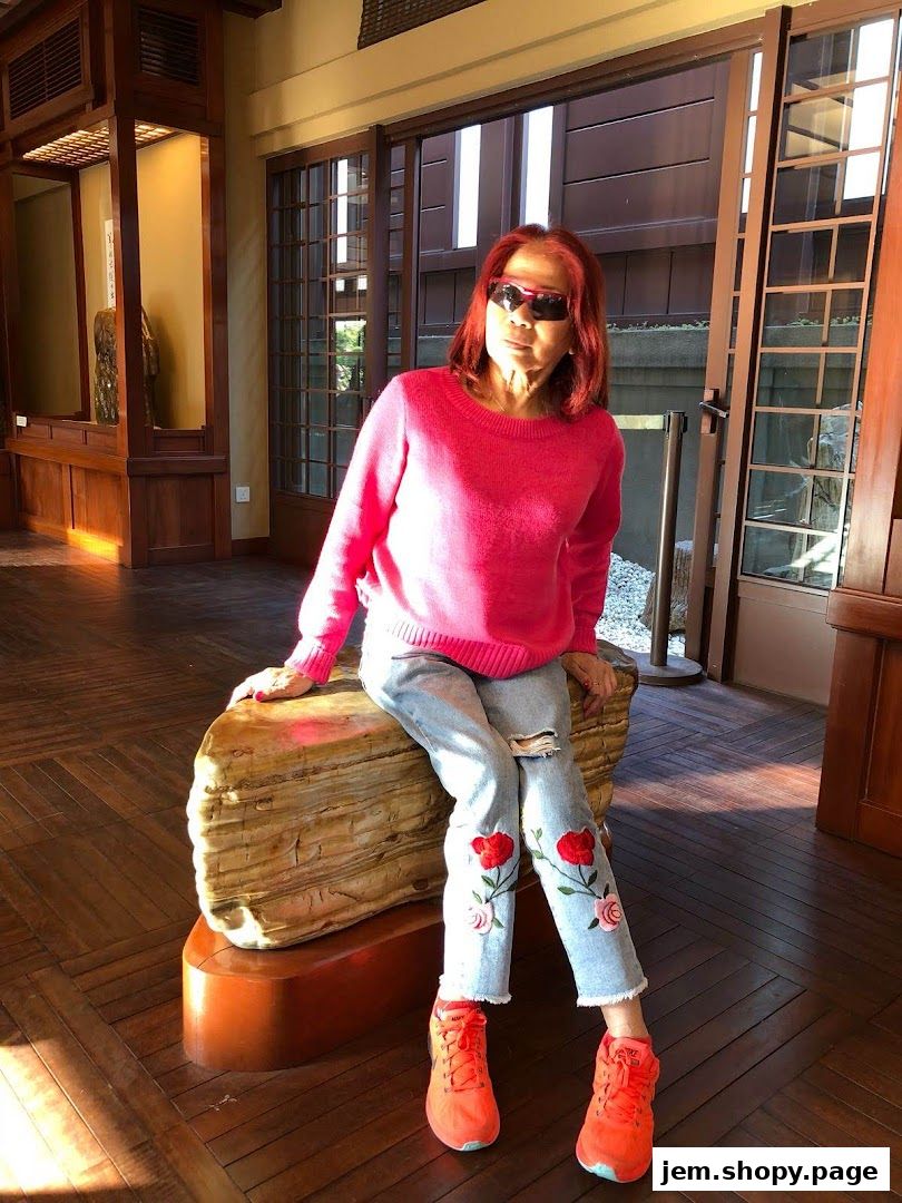 A woman with red hair and sunglasses sits on a large stone sculpture.