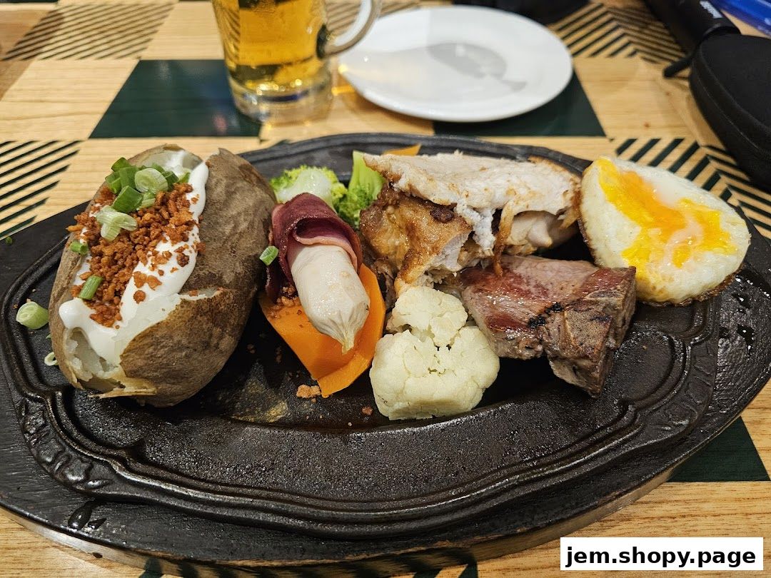 A hearty meal featuring a baked potato, sausage, steak, chicken, and egg, served with a beer.