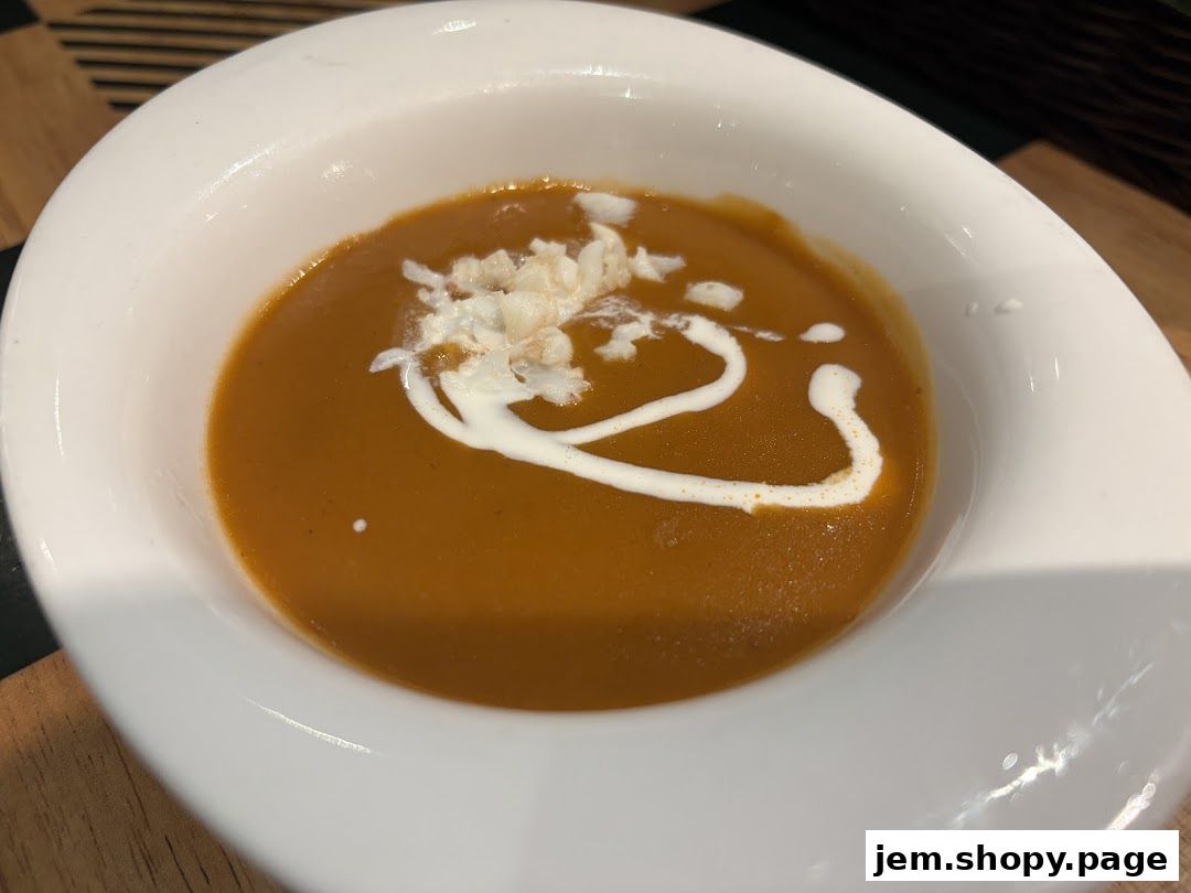 A close-up shot of a bowl of creamy pumpkin soup with a swirl of cream and shredded toppings.