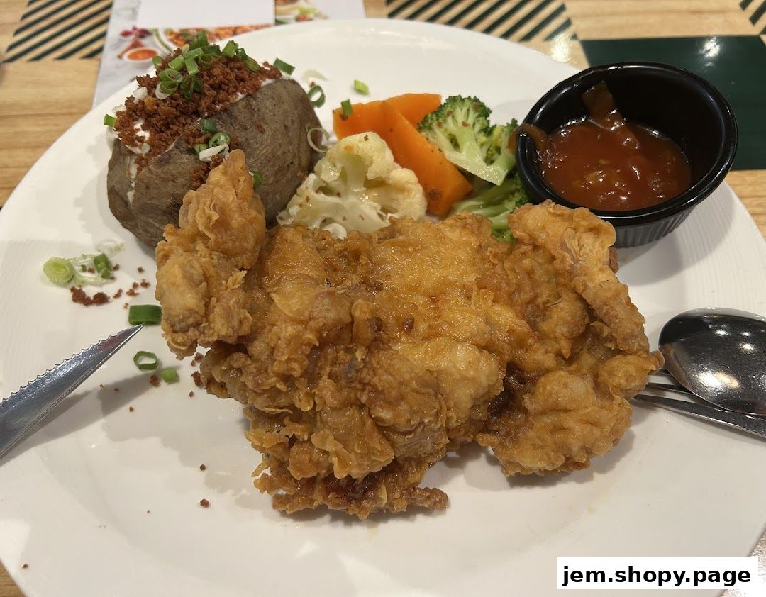A plate of crispy fried chicken with a baked potato and vegetables.