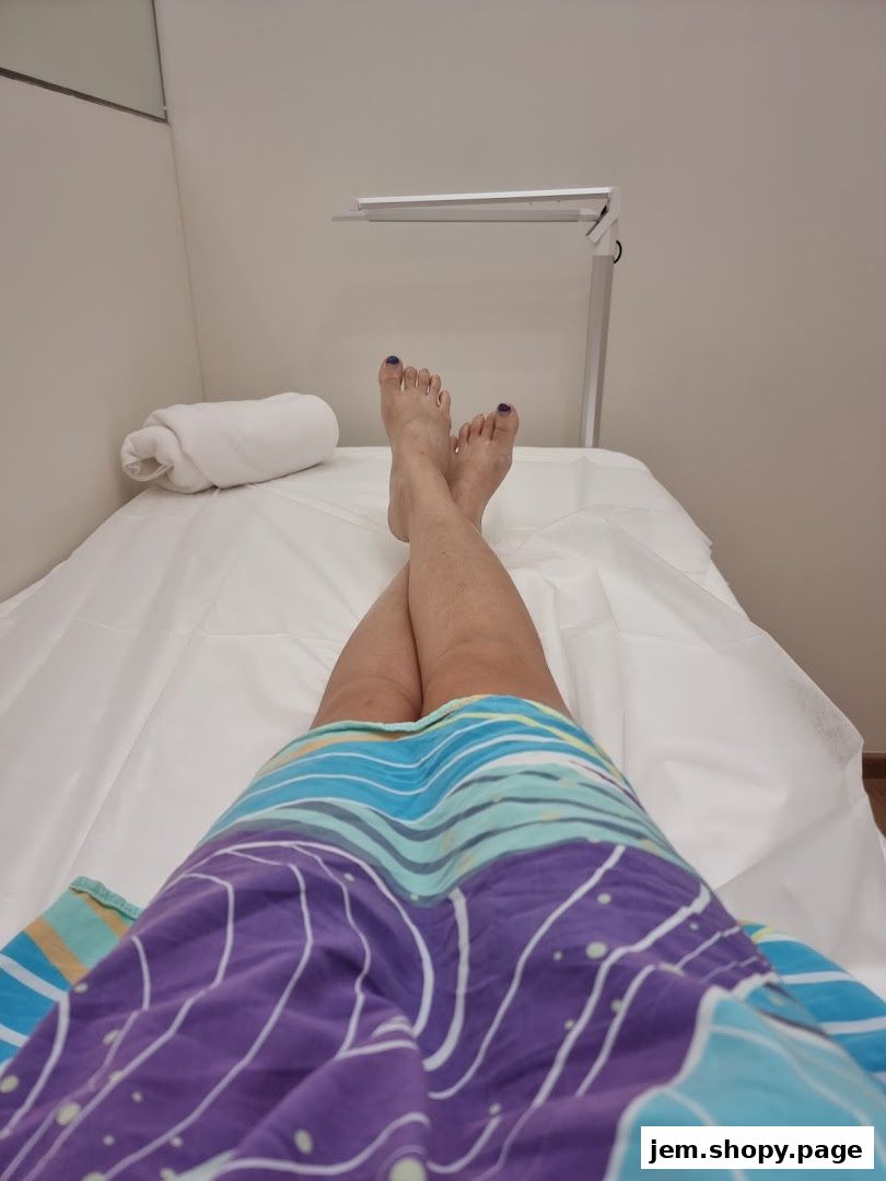 A person's legs and feet resting on a treatment bed with a lamp overhead.