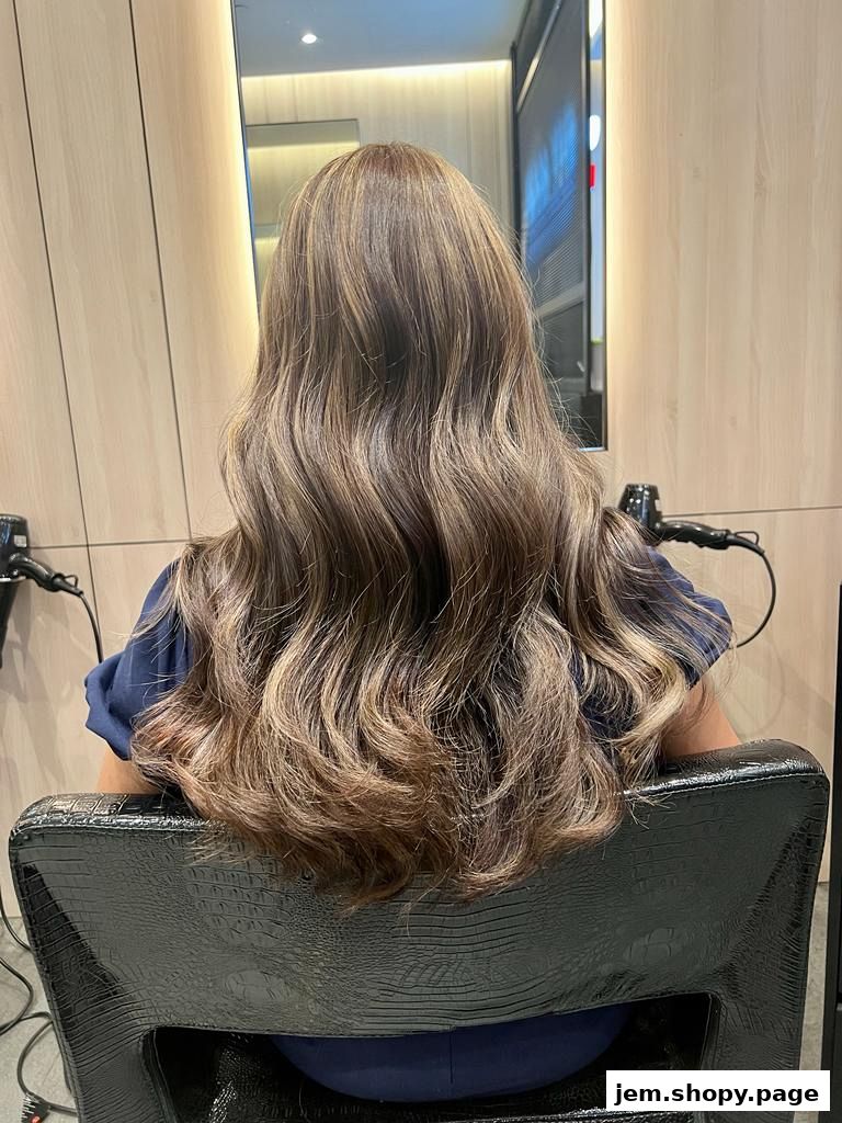 A person with long, wavy, highlighted hair sits in a salon chair.
