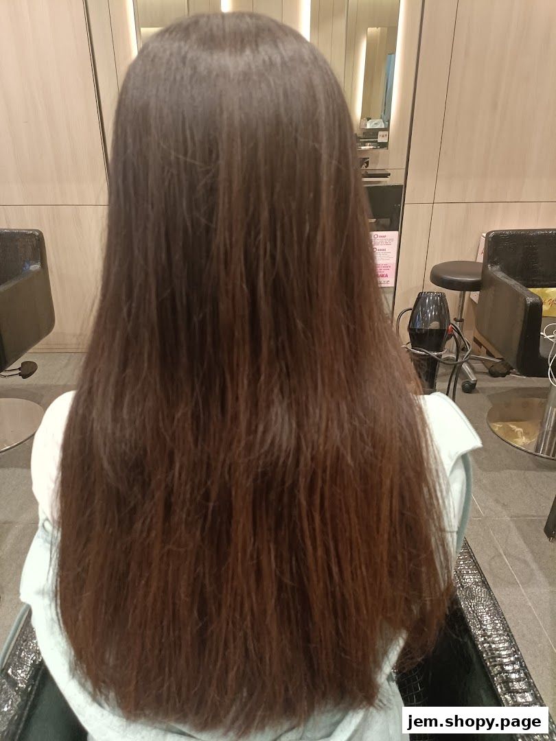 A person with long, dark brown hair sitting in a salon chair, viewed from behind.