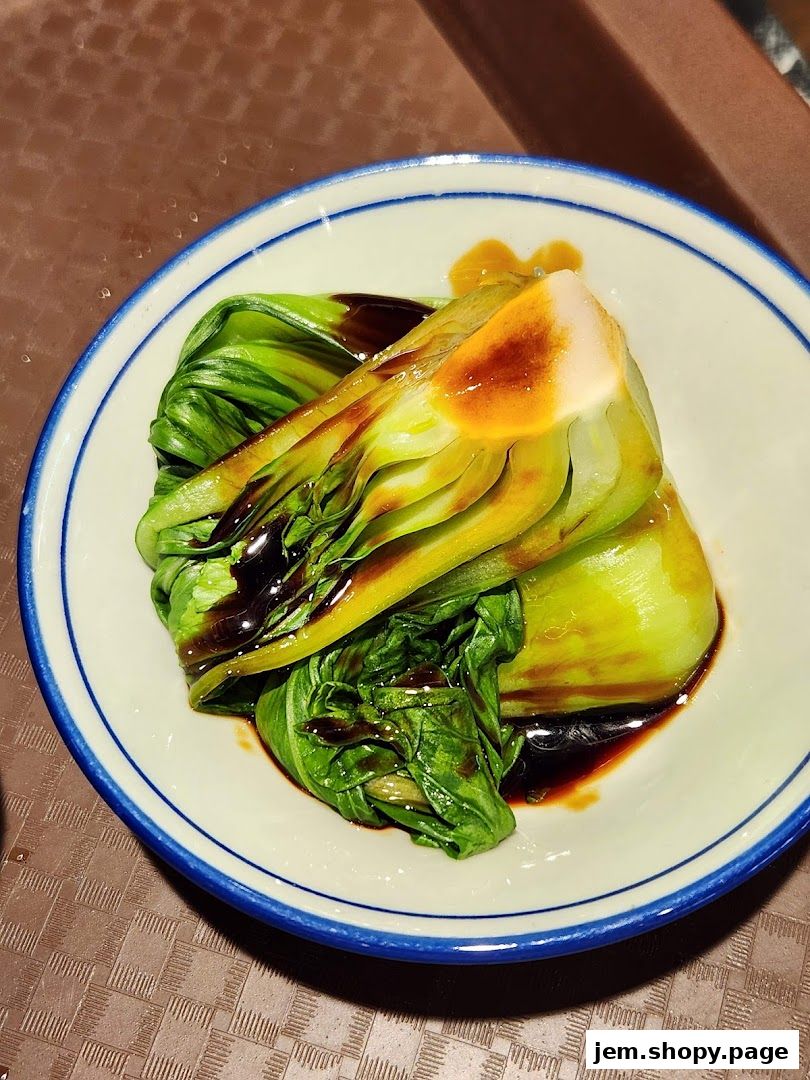 A close-up of a bowl of steamed bok choy drizzled with sauce.
