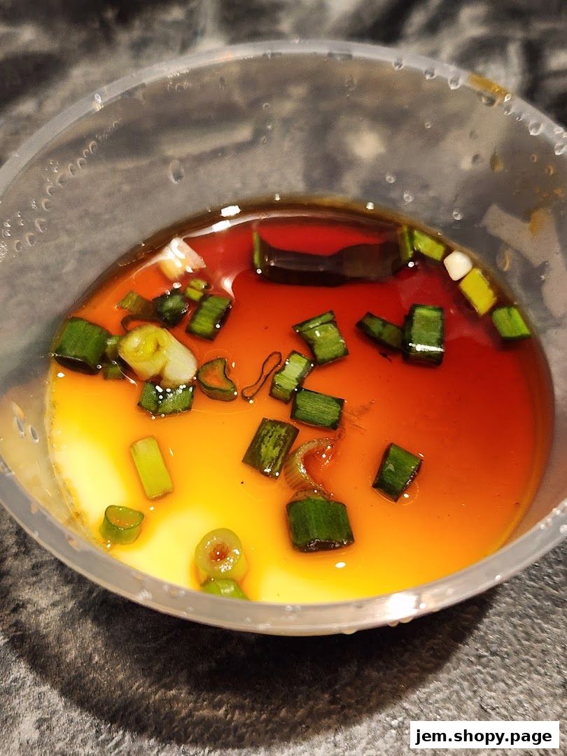 A close-up of a steamed egg dish with soy sauce and chopped scallions.