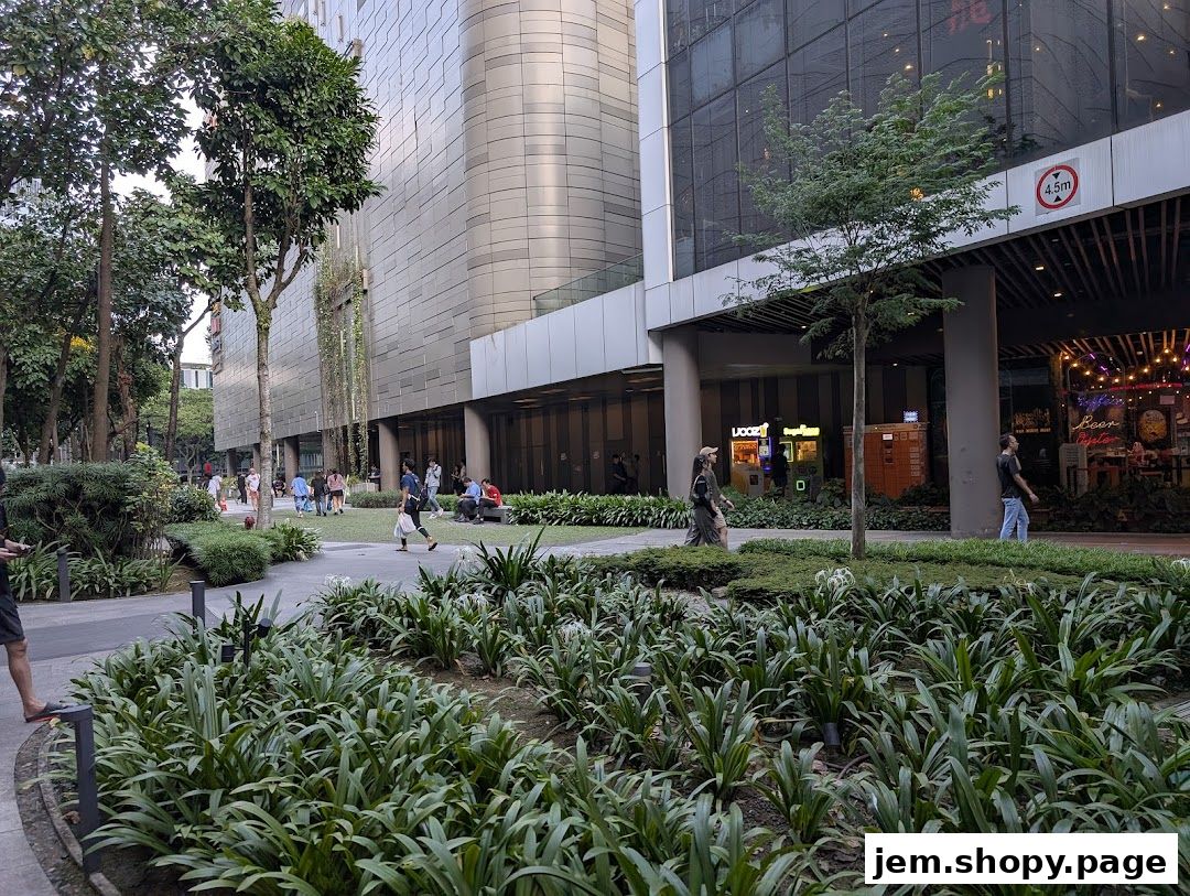People walking past shops and lush greenery in a modern urban setting.