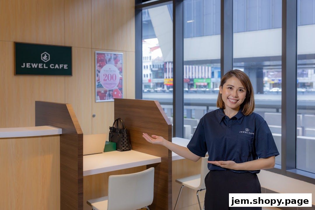 A smiling woman in a Jewel Cafe uniform gestures welcomingly in a modern cafe interior.