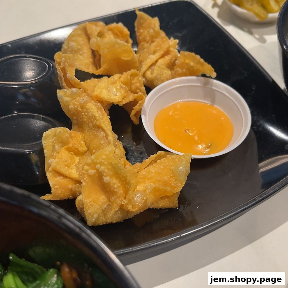 Crispy fried wontons served with a creamy orange dipping sauce on a black plate.