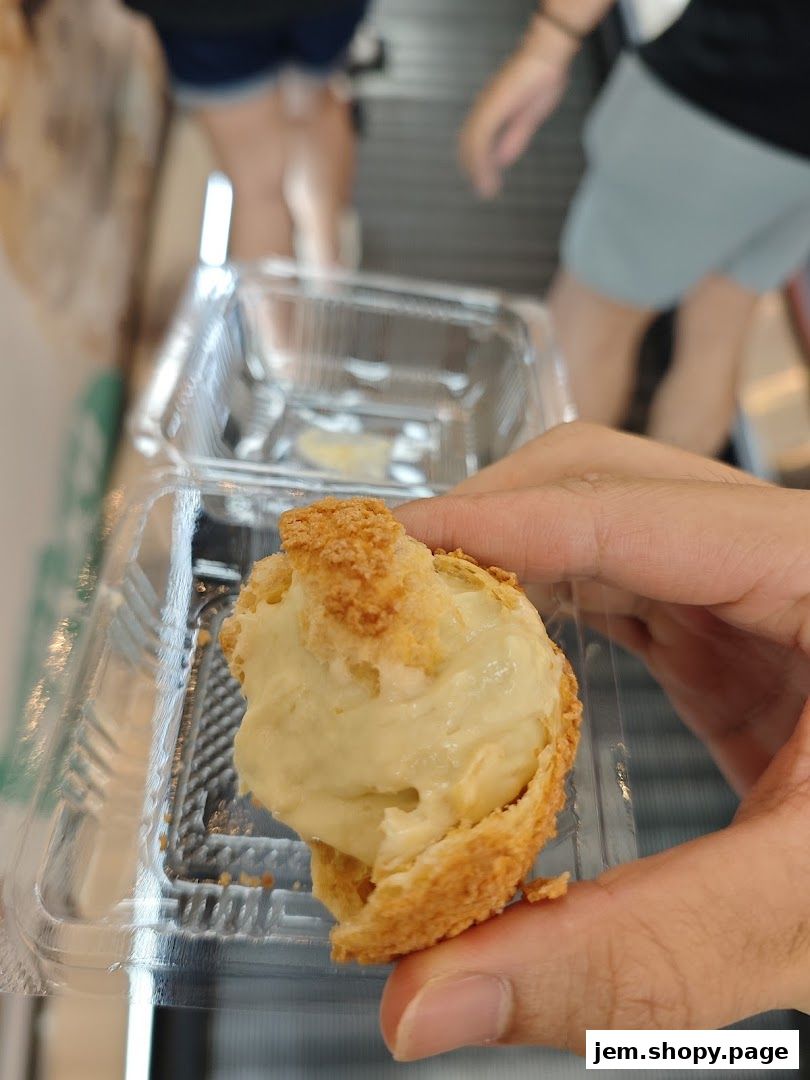 A hand holds a cream-filled pastry in a clear plastic container.