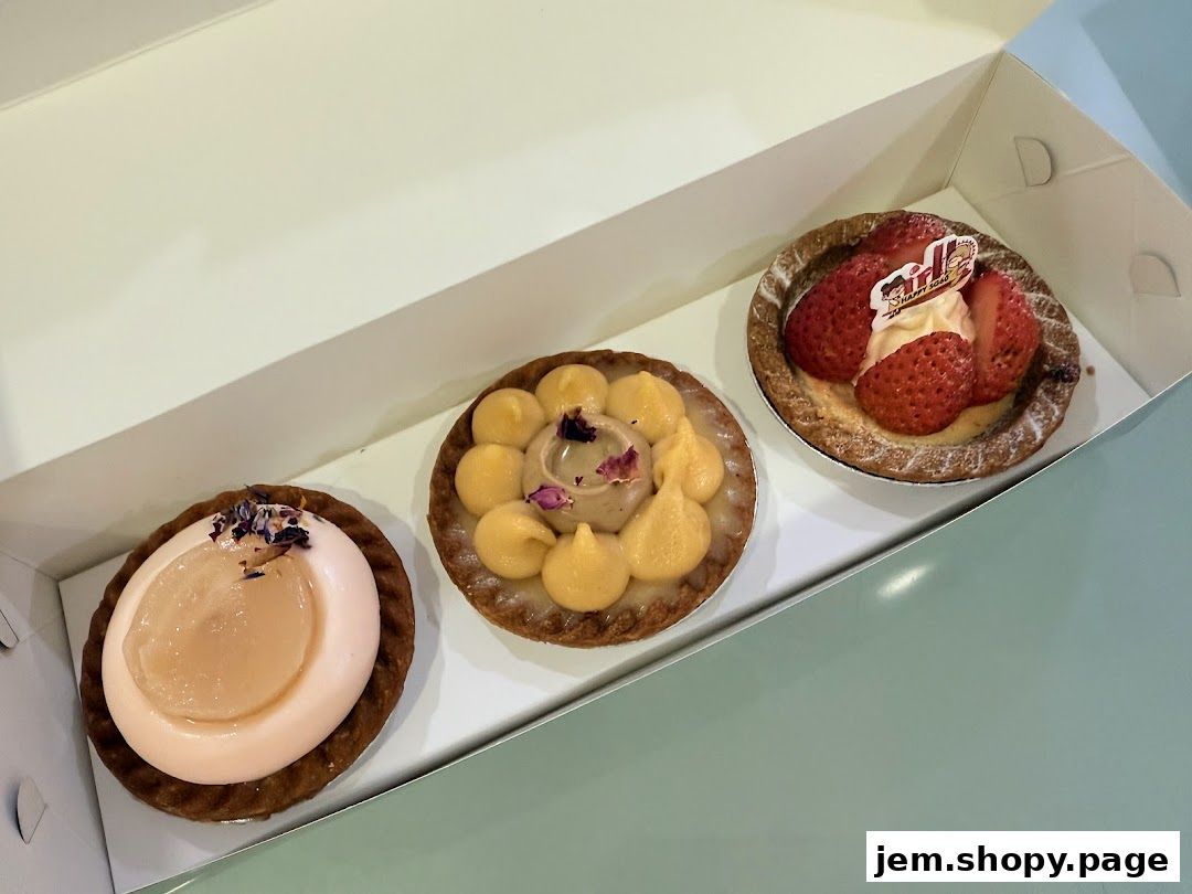 Three delicious tarts, one with strawberries, one with yellow cream, and one with pink cream and fruit.