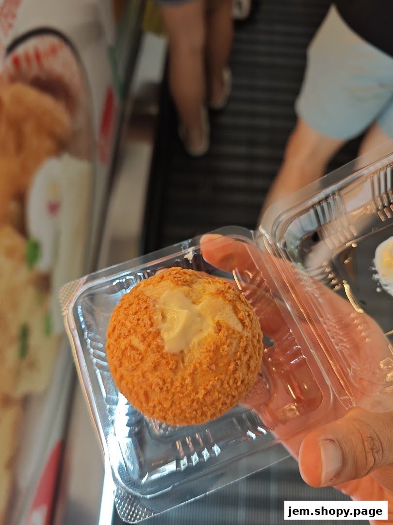 A hand holds a golden-brown, breaded pastry with a creamy filling.