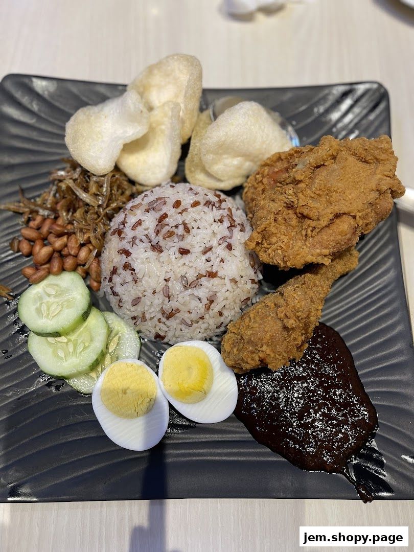 A plate of Nasi Lemak with fried chicken, rice, egg, cucumber, and crackers.
