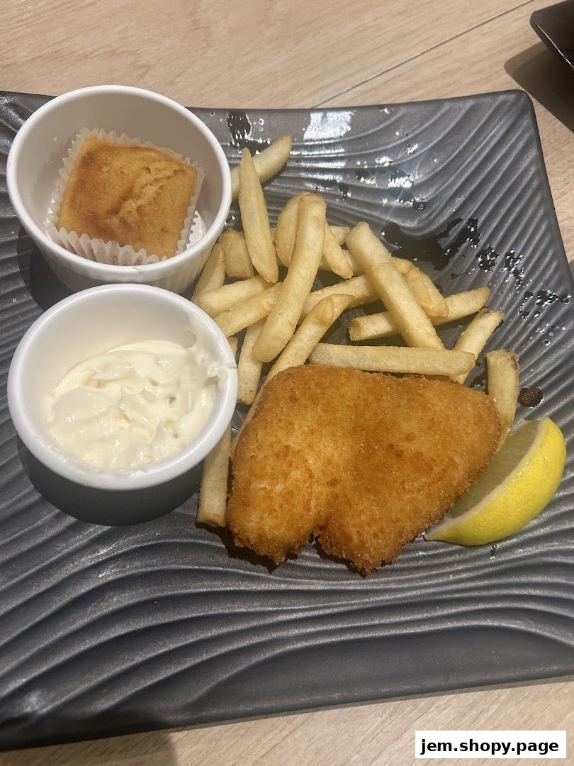 A plate of fish and chips with a side of sauce and a small bread.