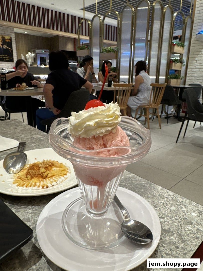 A strawberry ice cream sundae with whipped cream and a cherry, served in a glass sundae dish.