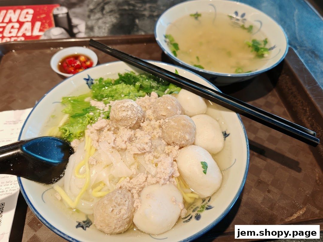 A bowl of noodle soup with meatballs, minced meat, and a side of soup.