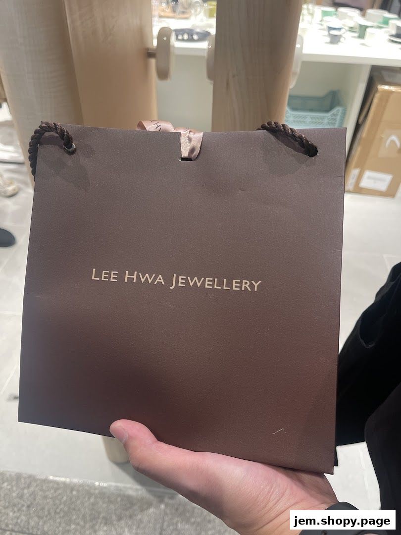 A hand holds a brown shopping bag with 'Lee Hwa Jewellery' logo.