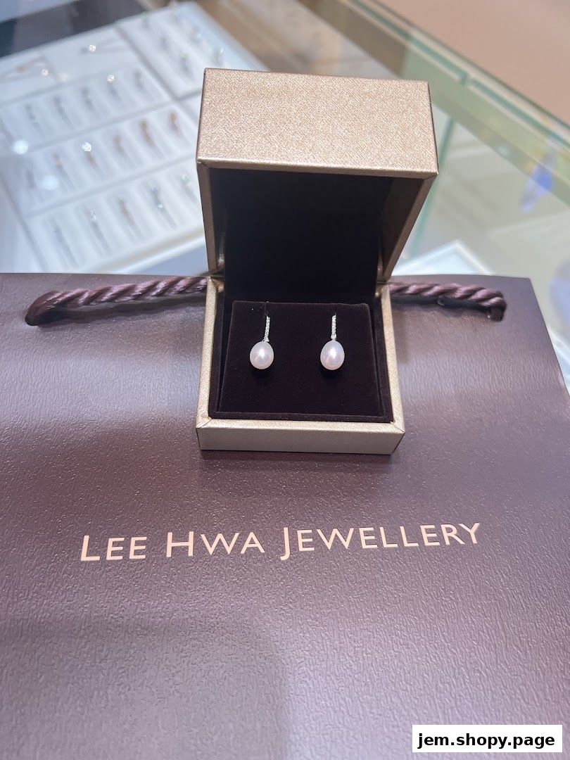 A jewelry box with pearl earrings sits on a Lee Hwa Jewellery shopping bag.
