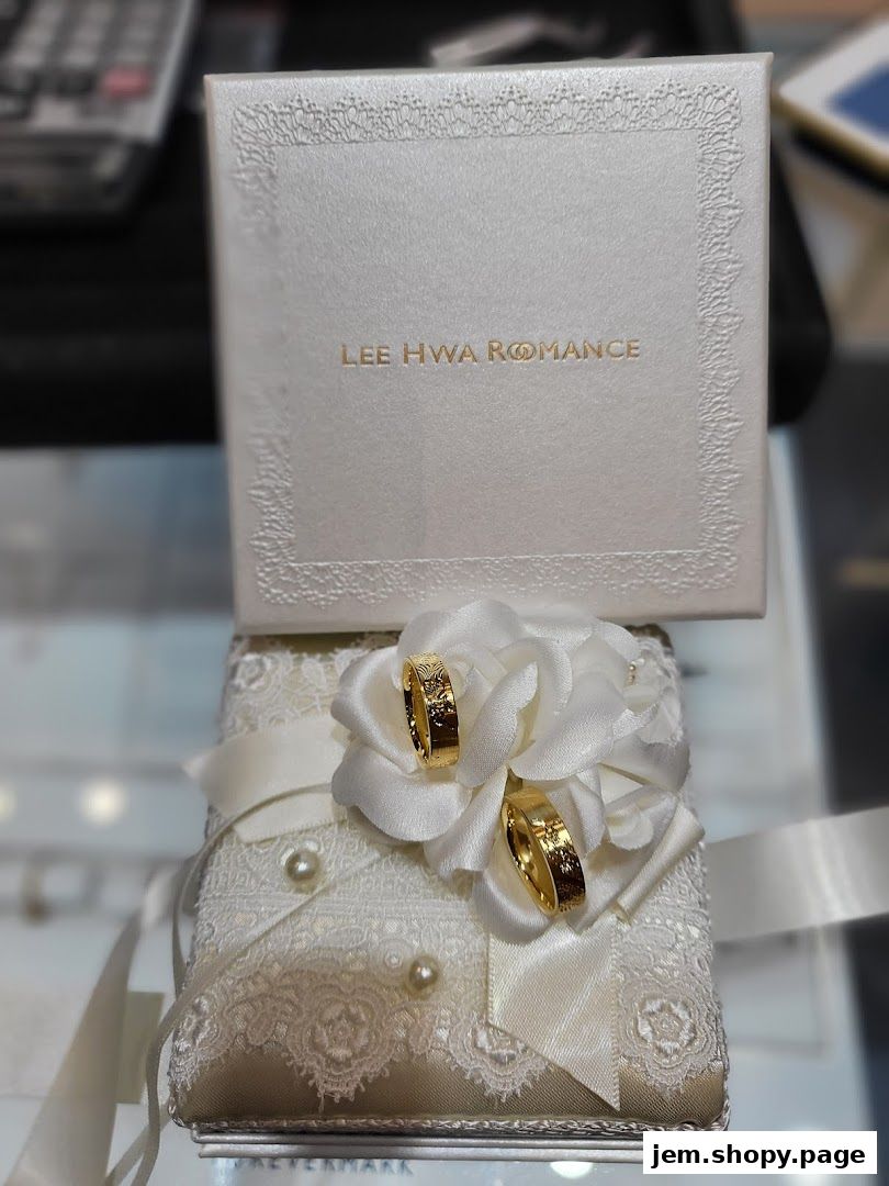 Two gold wedding rings displayed on a decorative cushion with a box from Lee Hwa Jewellery.
