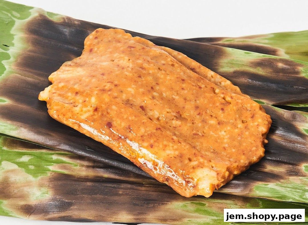 A close-up of a grilled otah fish cake wrapped in banana leaves.