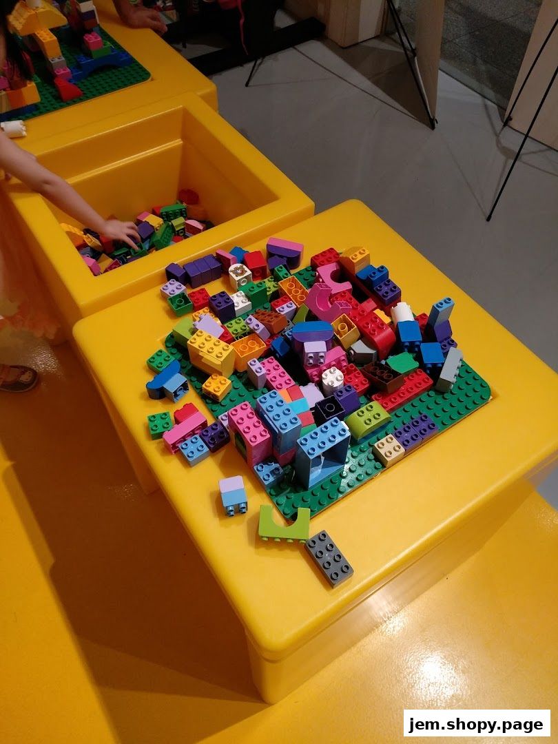 Children playing with colorful LEGO bricks on yellow tables in a store.