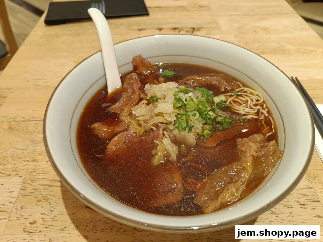 A close-up shot of a steaming bowl of beef noodle soup with tender beef and fresh scallions.