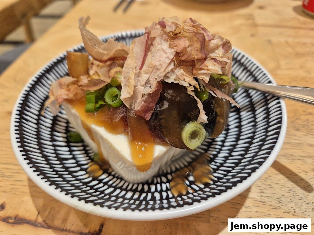 A close-up of a tofu dish topped with bonito flakes and scallions on a patterned plate.