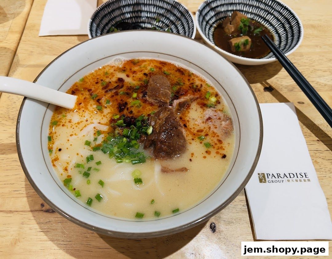 A bowl of hearty beef noodle soup with a side dish and chopsticks.
