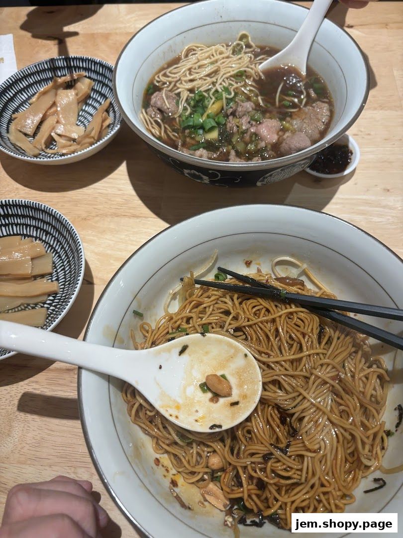 Two bowls of noodles and a side of bamboo shoots are served on a wooden table.