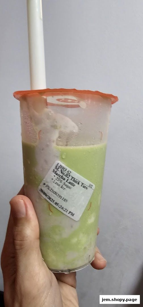A hand holds a LiHO TEA cup with a green and white layered drink and a label.