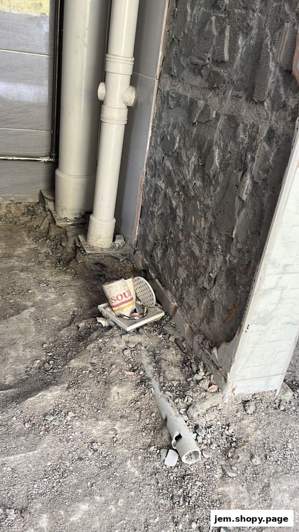 Construction debris and plumbing pipes are visible on the floor near a partially tiled wall.