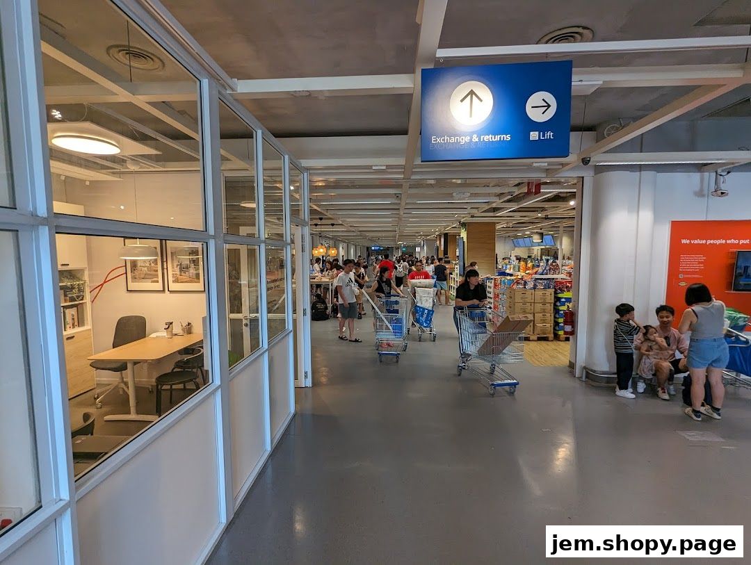 Interior view of a busy retail store with shoppers and shopping carts, featuring an office space and directional signs.