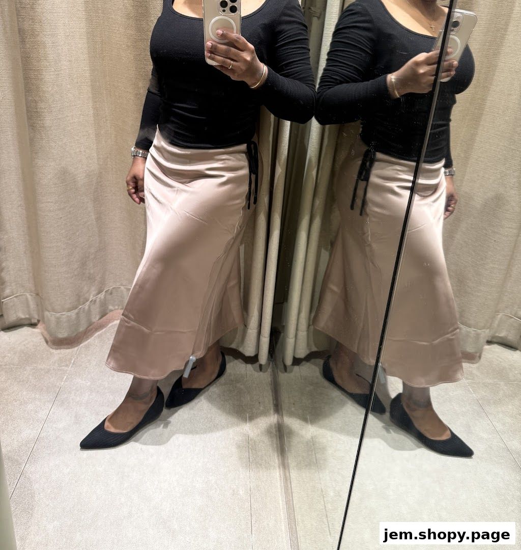 A woman tries on a satin skirt and black top in a fitting room.