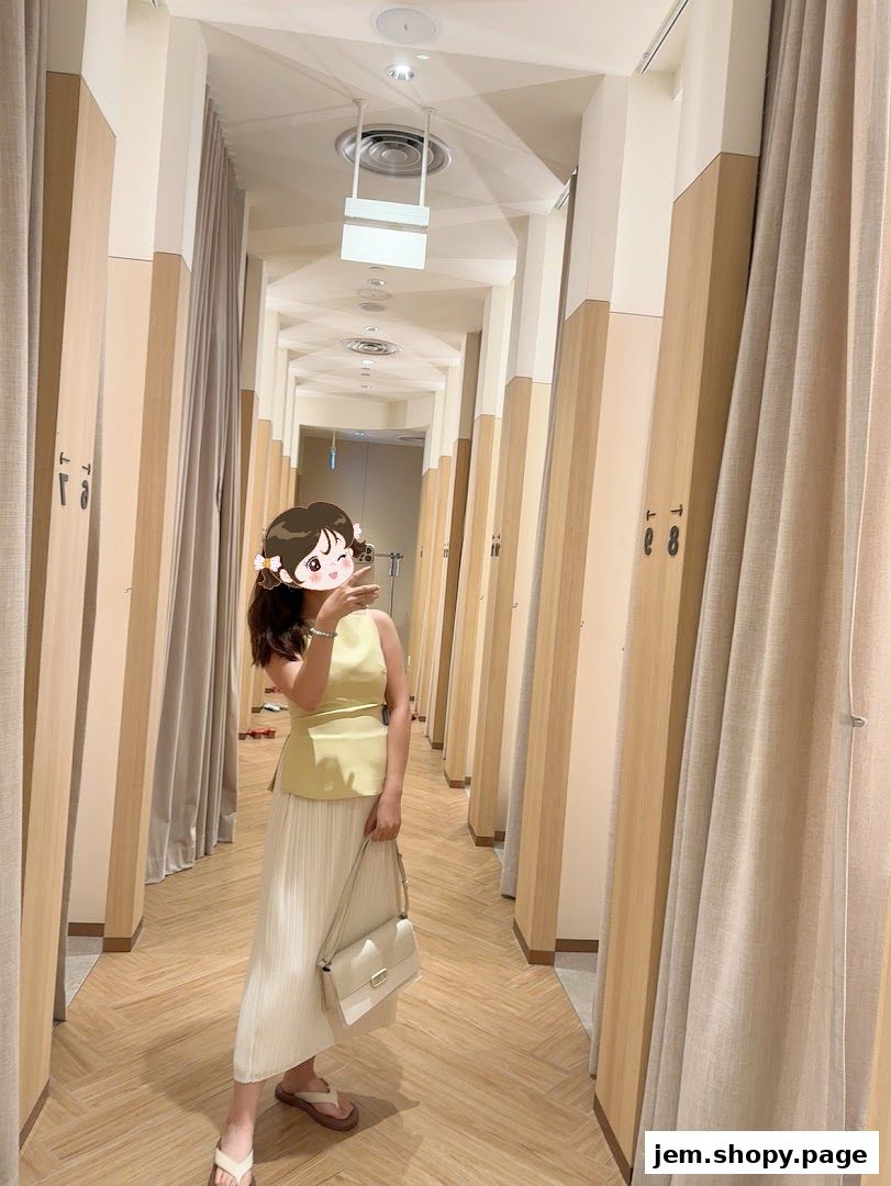 A woman takes a mirror selfie in a brightly lit fitting room with beige curtains.