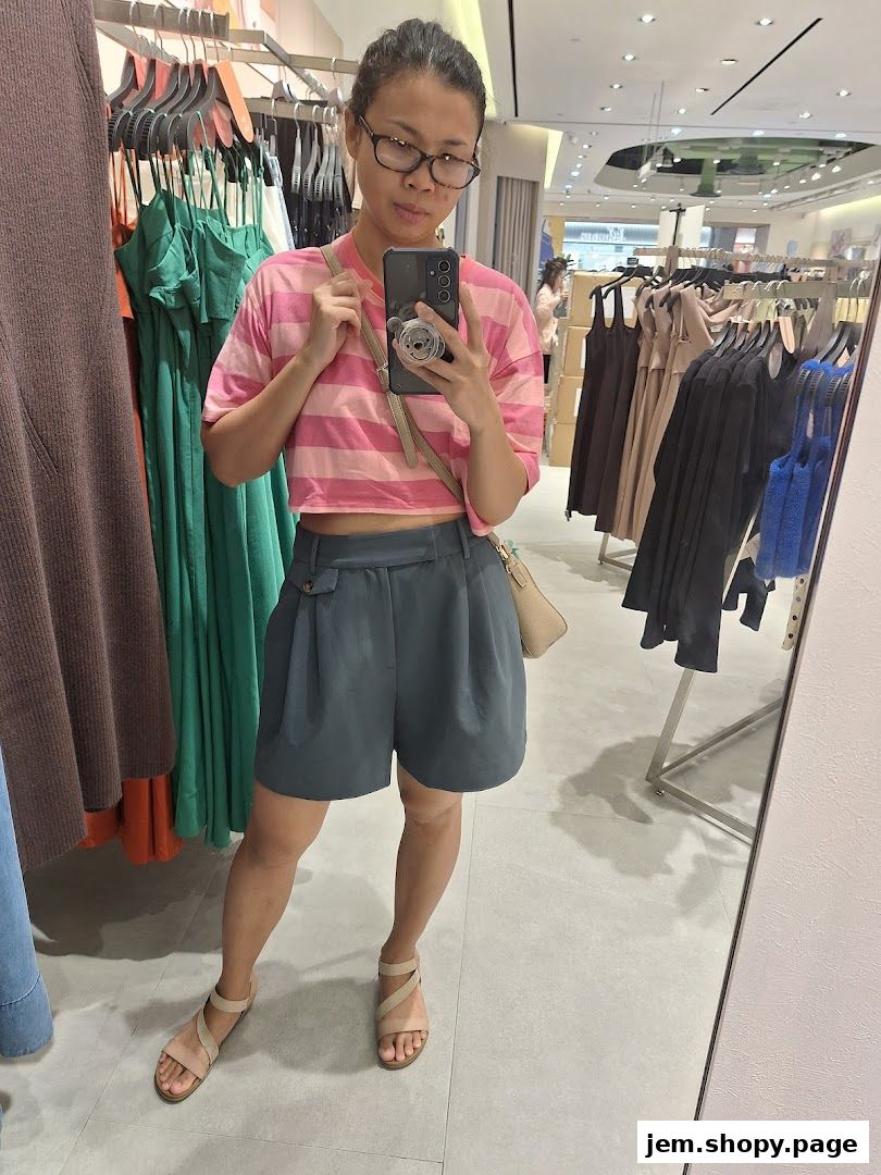A woman takes a mirror selfie in a clothing store, showcasing her outfit.