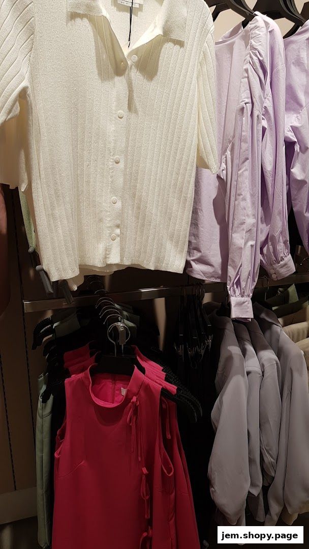 A display of women's clothing including a white ribbed top, lavender blouses, and a pink dress.