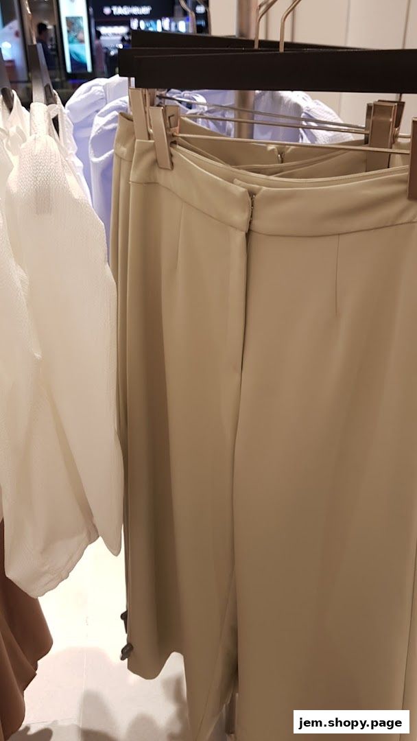 Close-up of beige trousers and white blouses on hangers in a clothing store.