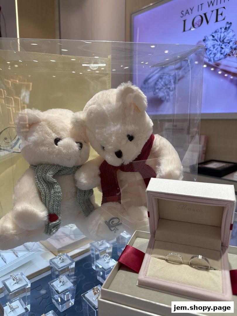 Two teddy bears in festive scarves sit near a display of engagement rings and wedding bands.