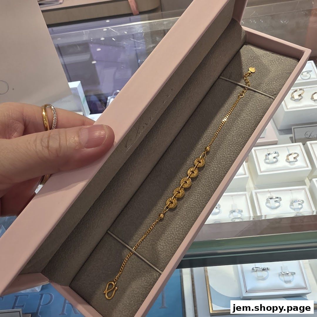 A hand holds a pink box revealing a delicate gold bracelet with circular links.