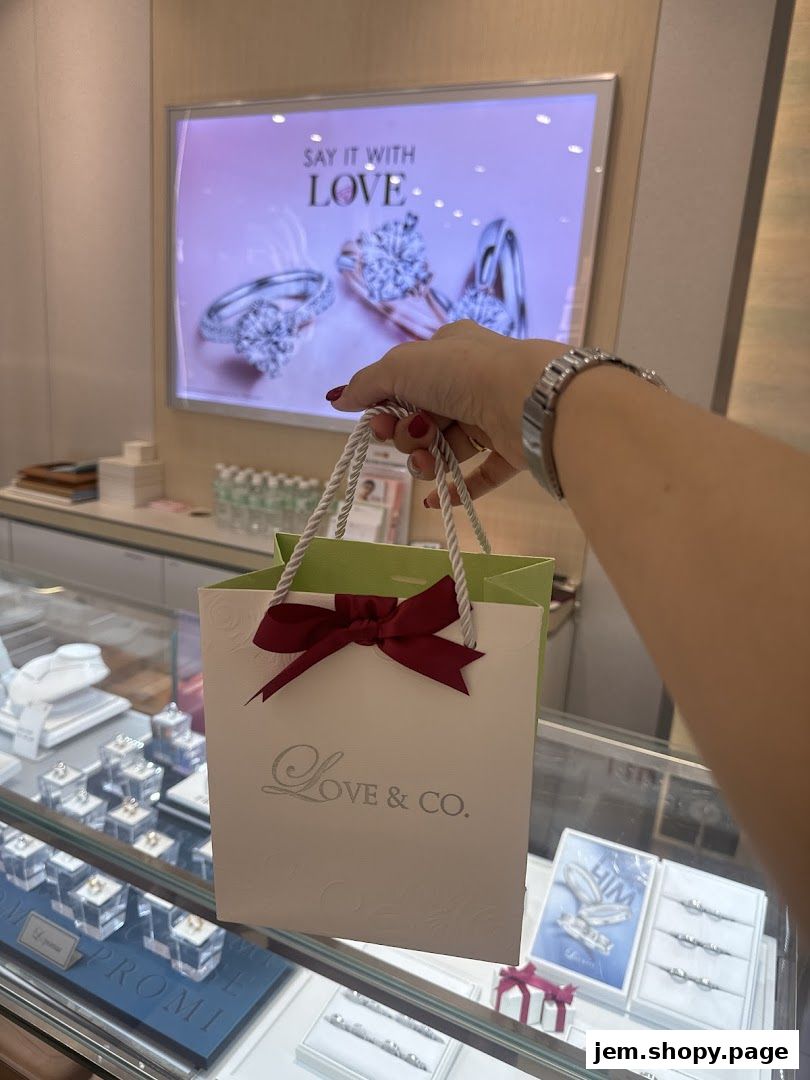 A hand holds a Love & Co. shopping bag in front of a display of diamond rings.