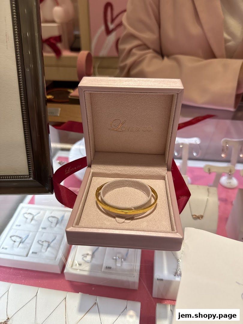 A gold bangle is displayed in an open pink jewelry box with other jewelry in the background.