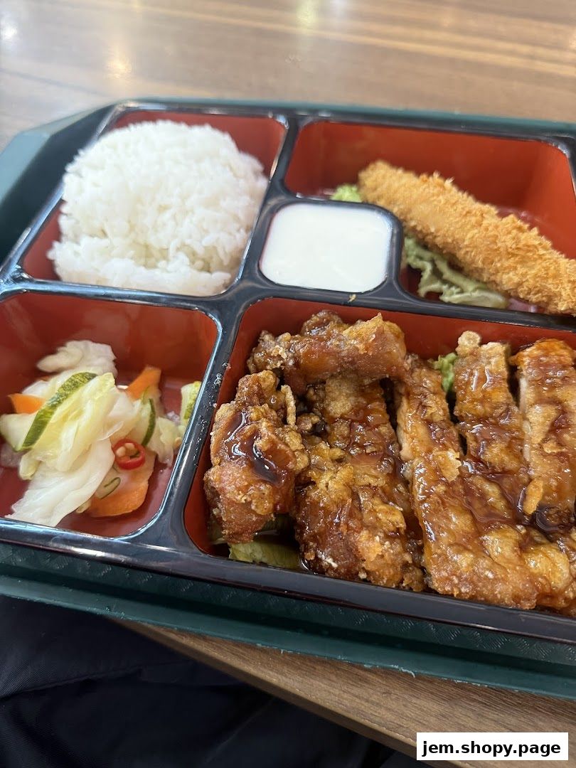 A bento box with rice, fried chicken, pickled vegetables, and a fried shrimp.