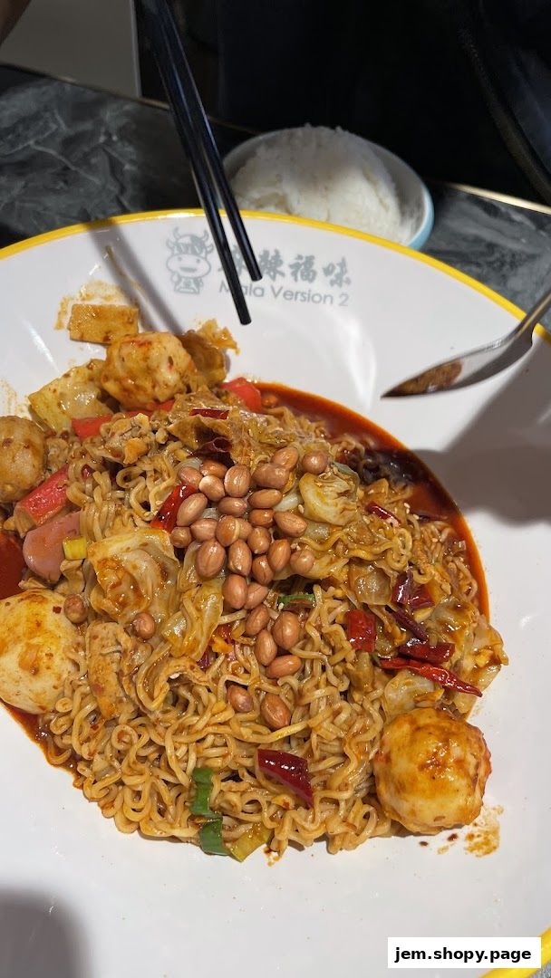 A close-up of a spicy noodle dish with peanuts, meatballs, and vegetables.