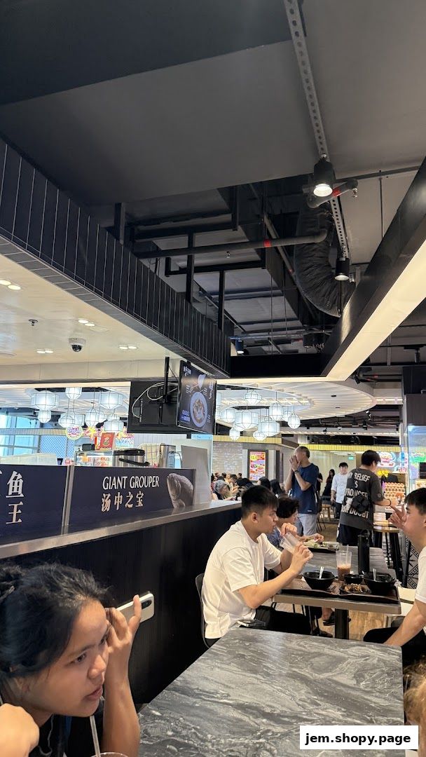Diners enjoy meals at tables in a bustling food court with a "Mala Version 2" stall visible.