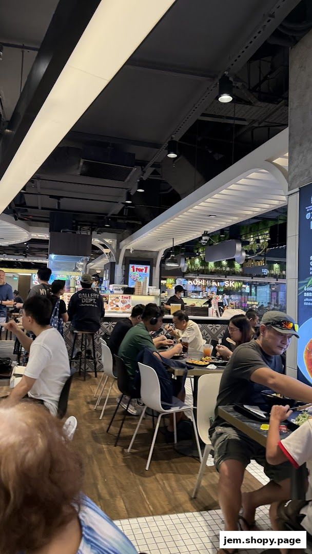 Diners enjoying meals at tables inside a bustling food court with various food stalls visible.