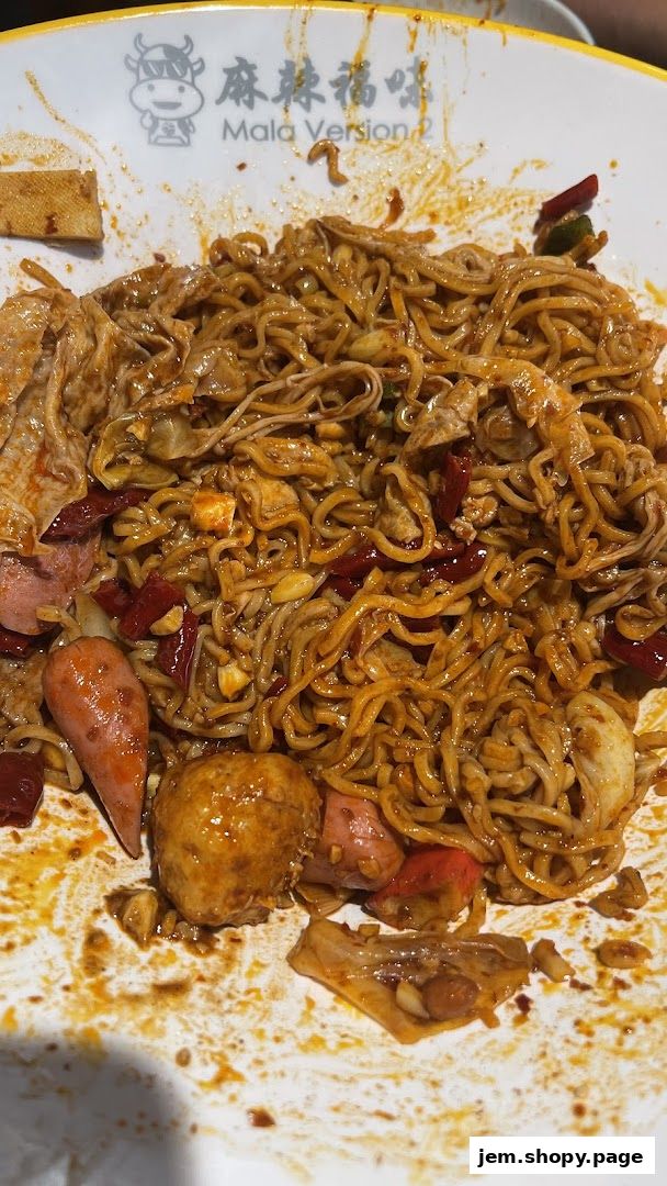 A close-up of a bowl of spicy noodles with various toppings like sausages and meatballs.