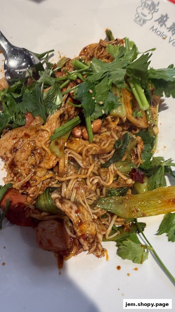 A close-up of a spicy mala dish with noodles, meat, vegetables, and peanuts.