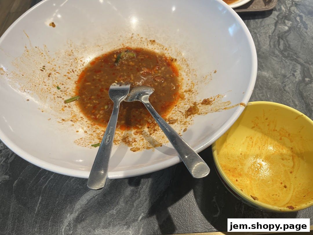 Two dirty bowls with leftover sauce and utensils on a dark marbled surface.
