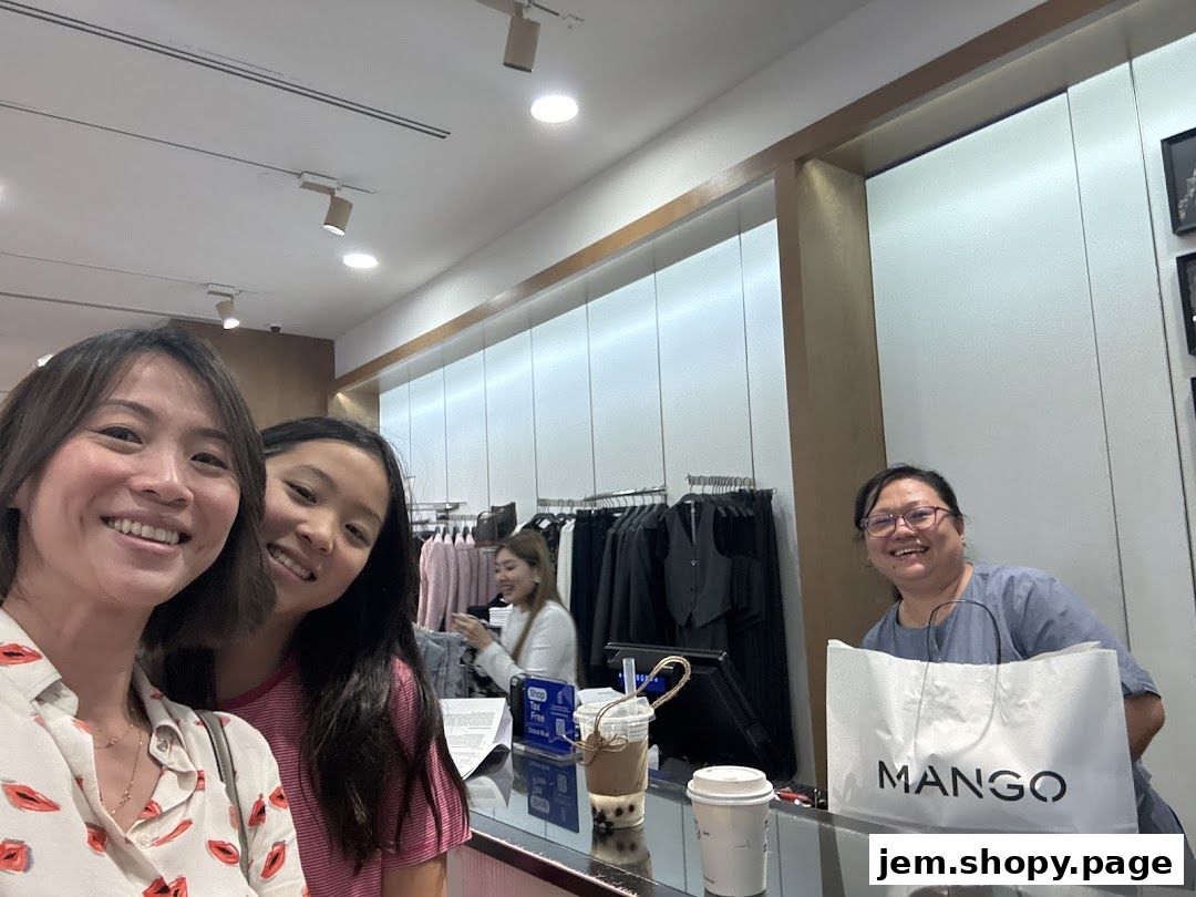 Two women and a cashier smile at the camera inside a MANGO clothing store.