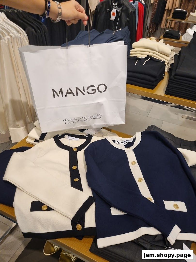 A person holds a MANGO shopping bag in front of displayed clothing items.